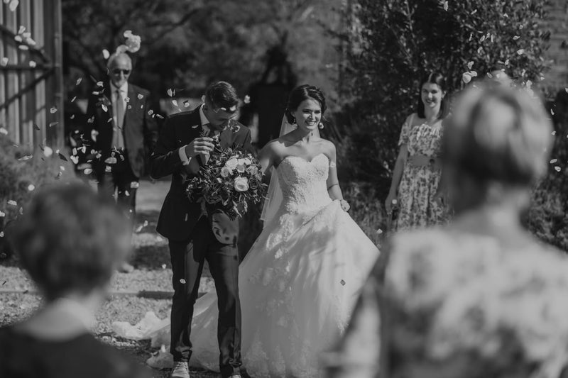 Black and white photograph of a bride and groom walking down an aisle with guests in the foreground.