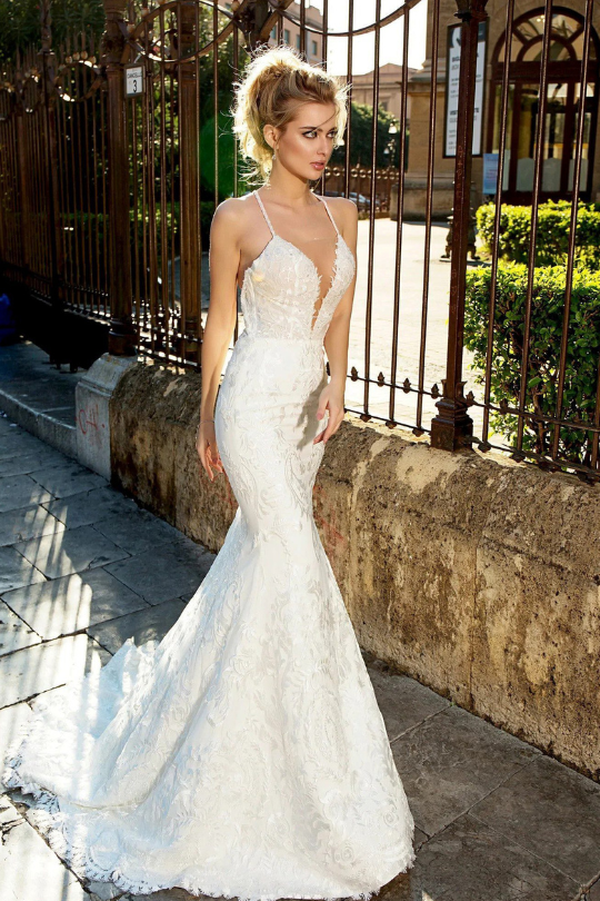 Woman in a white wedding dress standing outdoors near a wrought iron gate.